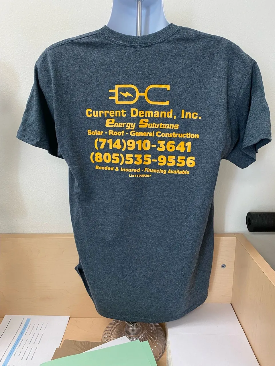 Heather navy tee printed in gold with the Current Demand, Inc. Energy Solutions logo and phone numbers