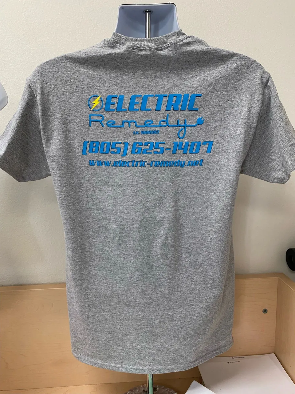 Gray tee with the Electric Remedy logo, phone number and website printed in blue on the back