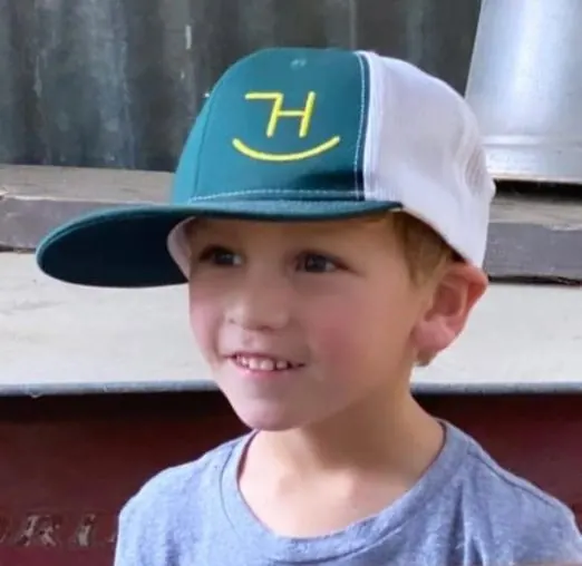 Young boy wearing a green and white trucker hat with a yellow embroidered H logo
