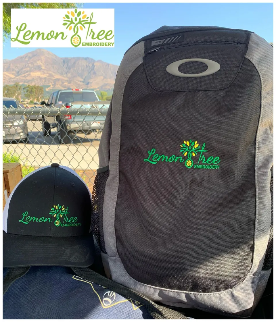 Black backpack and cap embroidered with the Lemon Tree Embroidery logo, outdoors