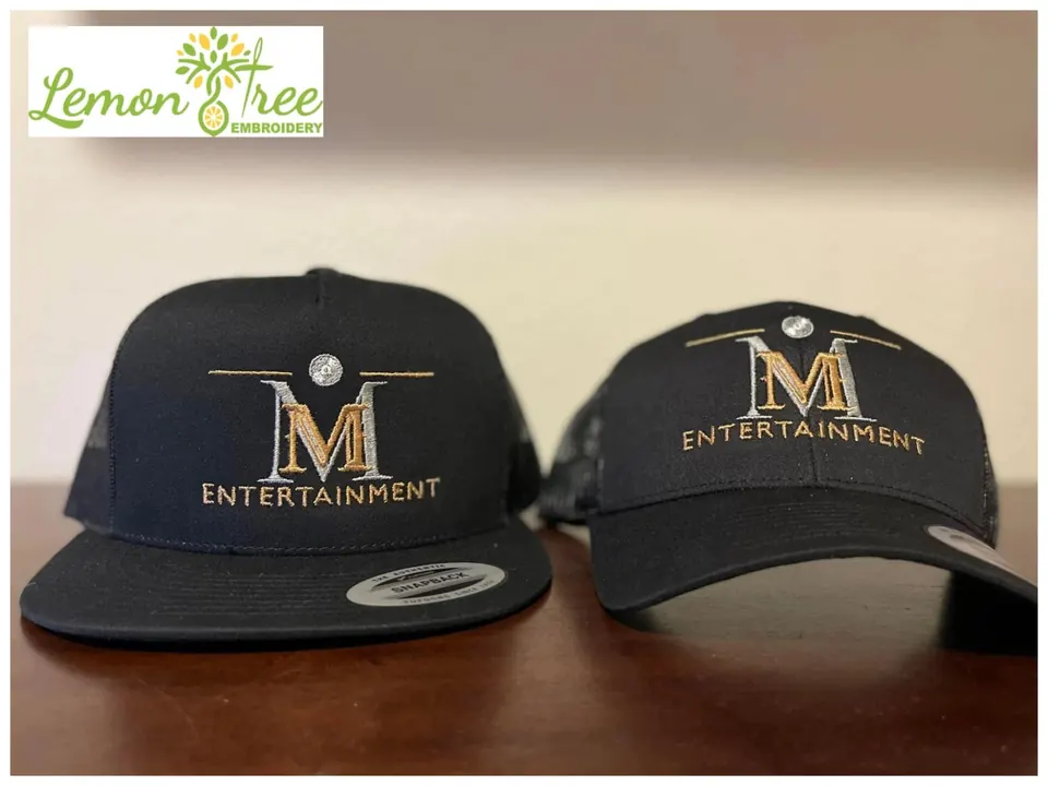 Two black snapback hats embroidered with the M Entertainment logo in gold