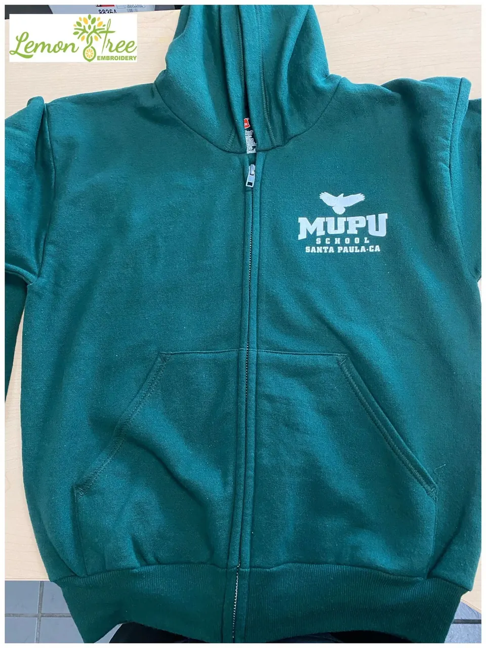 Teal zip hoodie printed with a small MUPU School logo on the chest